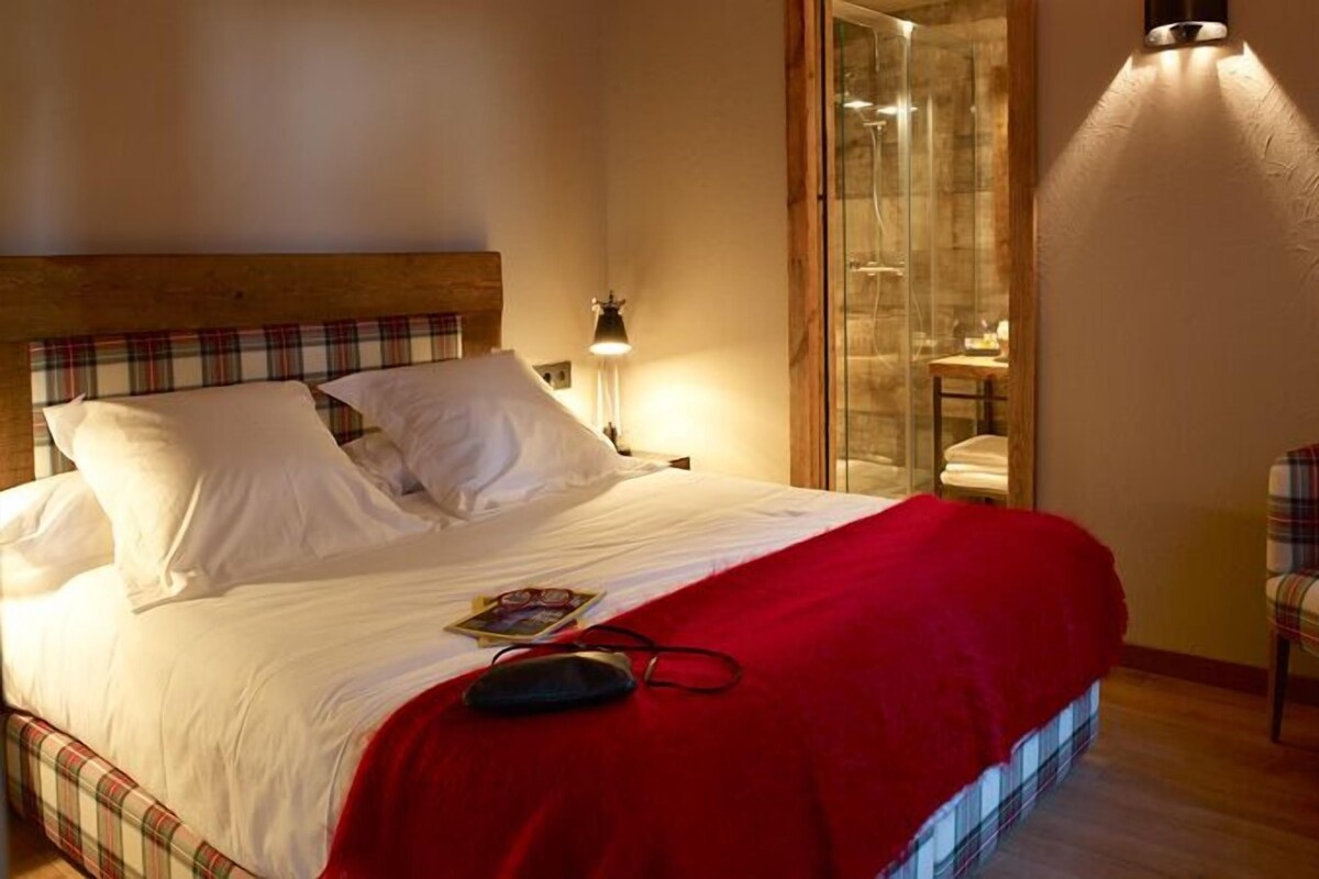 A hotel room with a bed, a chair, a nightstand, and a glass shower enclosure.