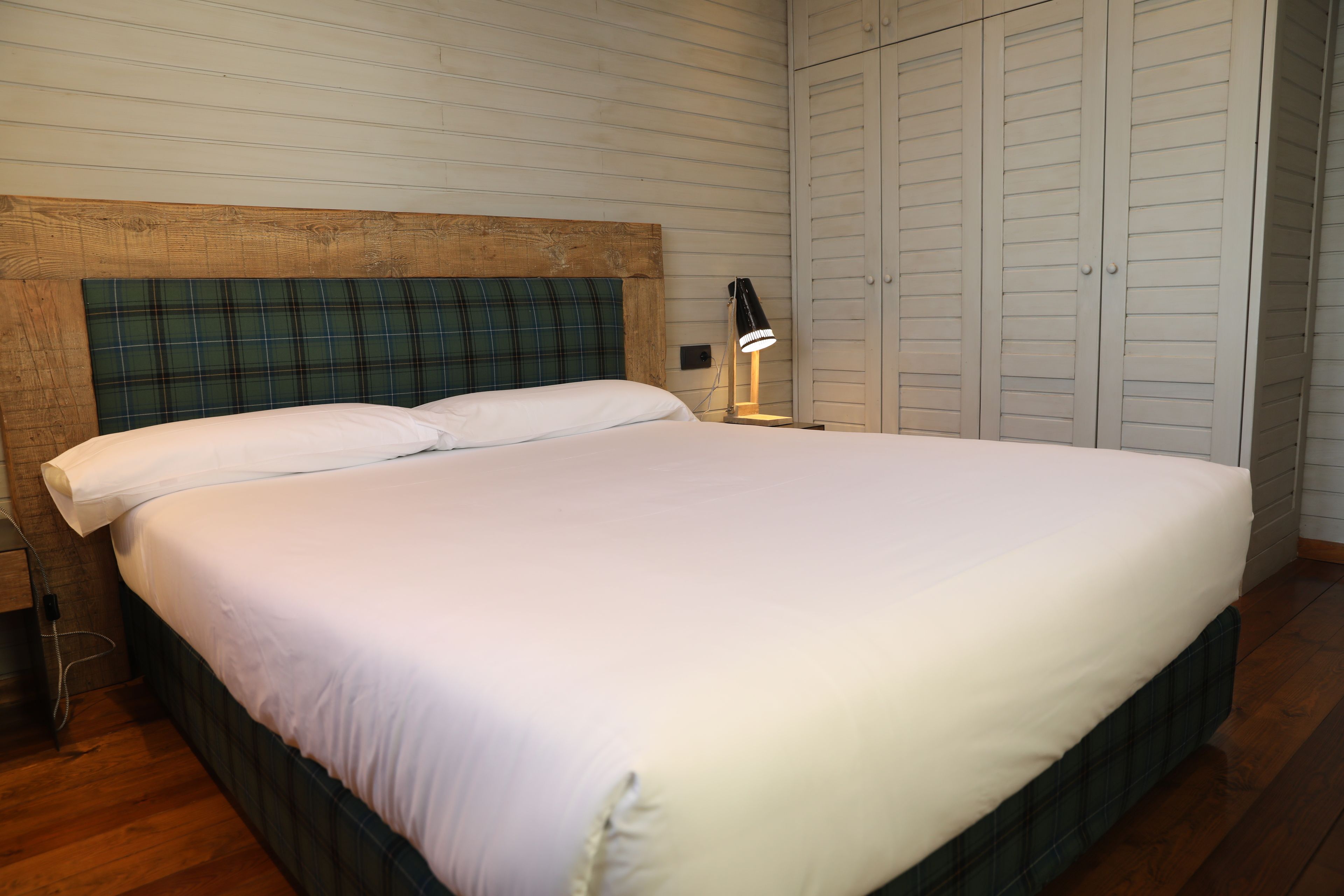 Una cama con cabecera de cuadros, ropa de cama blanca y una lámpara de noche.