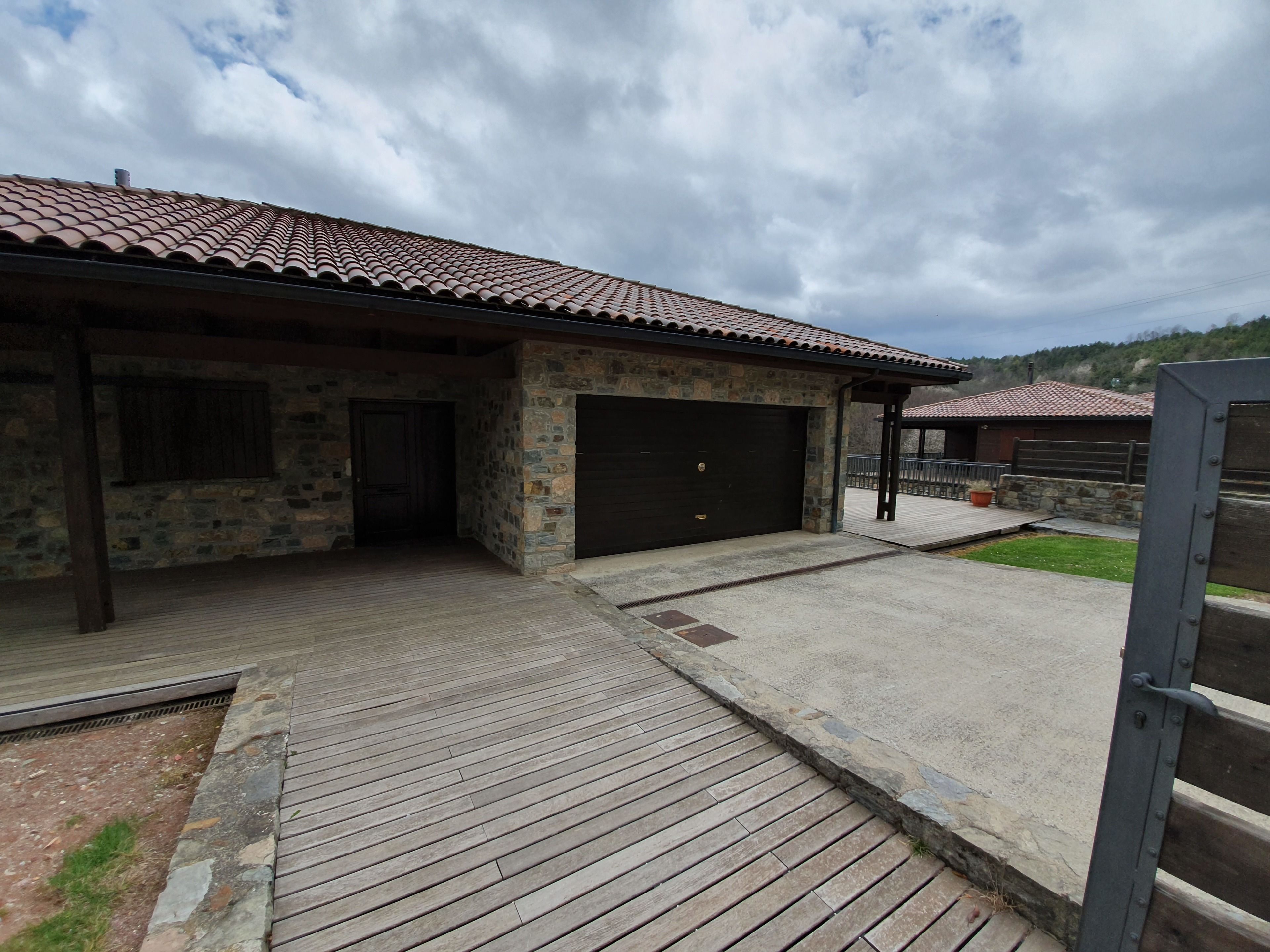 Une construction en pierre avec un toit en tuiles, un garage et un patio couvert.