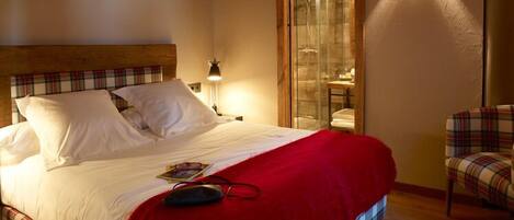 Una habitación de hotel con cama, sillón y cabina de ducha de vidrio.