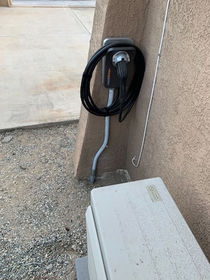 An outdoor electric vehicle charging station attached to a concrete wall.