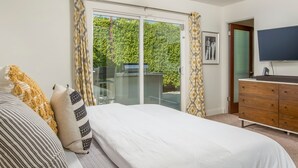 A bedroom with a bed, a dresser, a TV, and a sliding glass door leading to a balcony. - Sunny Palms at Warm Sands - Designer Pool Home (Palm Springs)