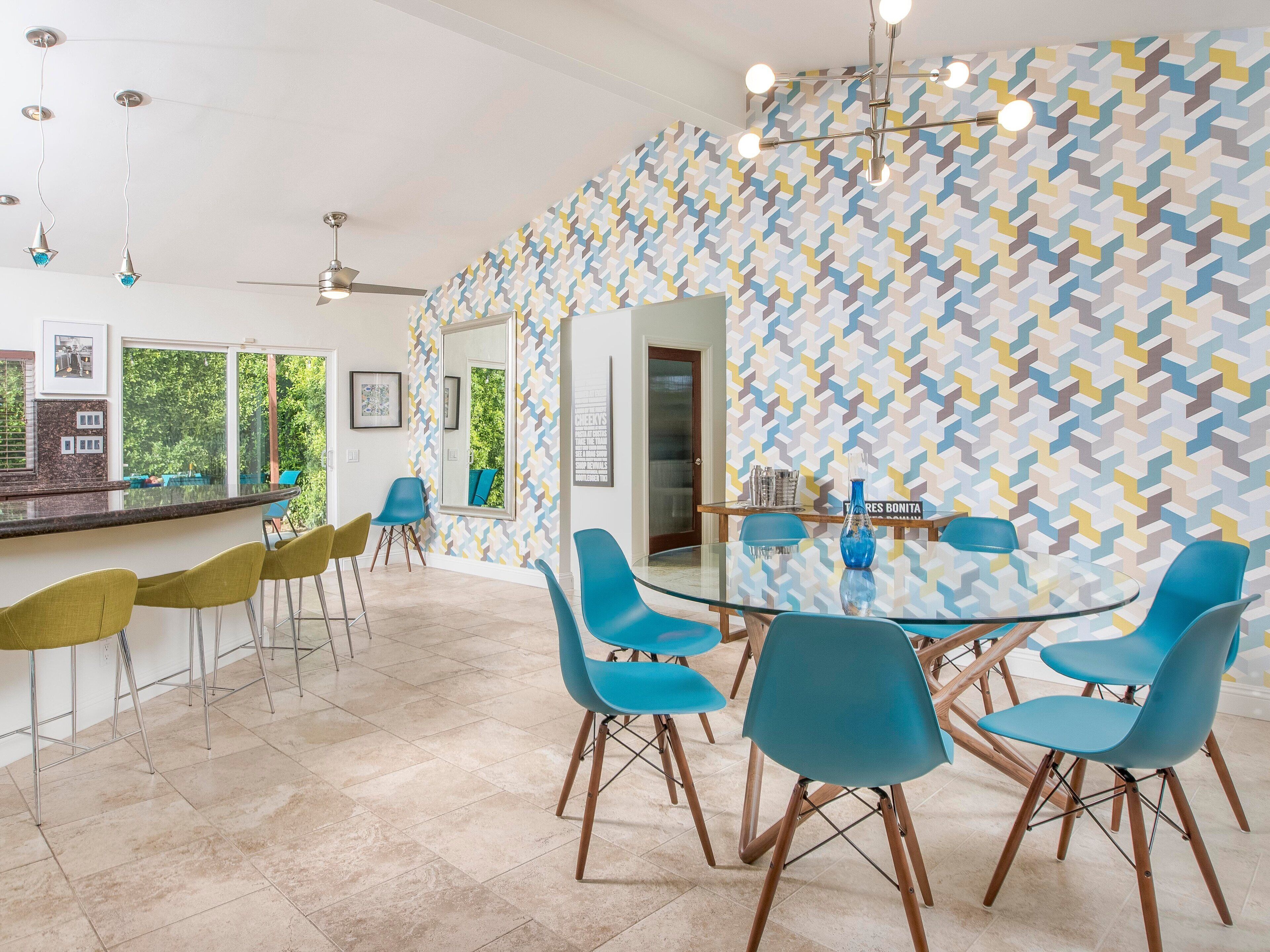 Een moderne eetruimte met een glazen tafel, blauwe stoelen en een behang met een patroon.