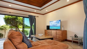 A modern living room with a brown sofa, a coffee table, a TV on a wooden cabinet, and a glass table. - Boutique 3BR Pool Villa Bianca NaiHarn (Rawai)