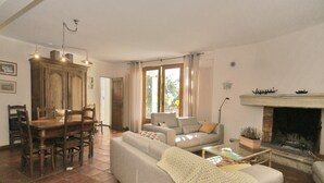 A living room with a sofa, a dining table with chairs, a fireplace, and a large window with curtains. - Villa in Crillon-le-Brave near Mont Ventoux (Crillon-le-Brave)