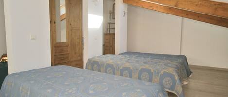 Une chambre avec deux lits, des poutres en bois au plafond et une armoire en bois.