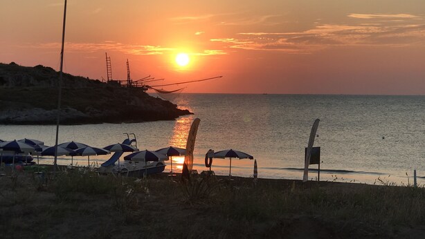 Ein Sonnenuntergang über einem Strand mit Sonnenschirmen und einem Steg.