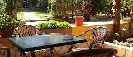 An outdoor patio with a table and chairs, surrounded by potted plants and a stone floor.