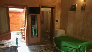 Ein Zimmer mit einem Bett, einem Tisch mit Obstmuster-Tischdecke, einem kleinen Fernseher und einer Tür zu einem Badezimmer.