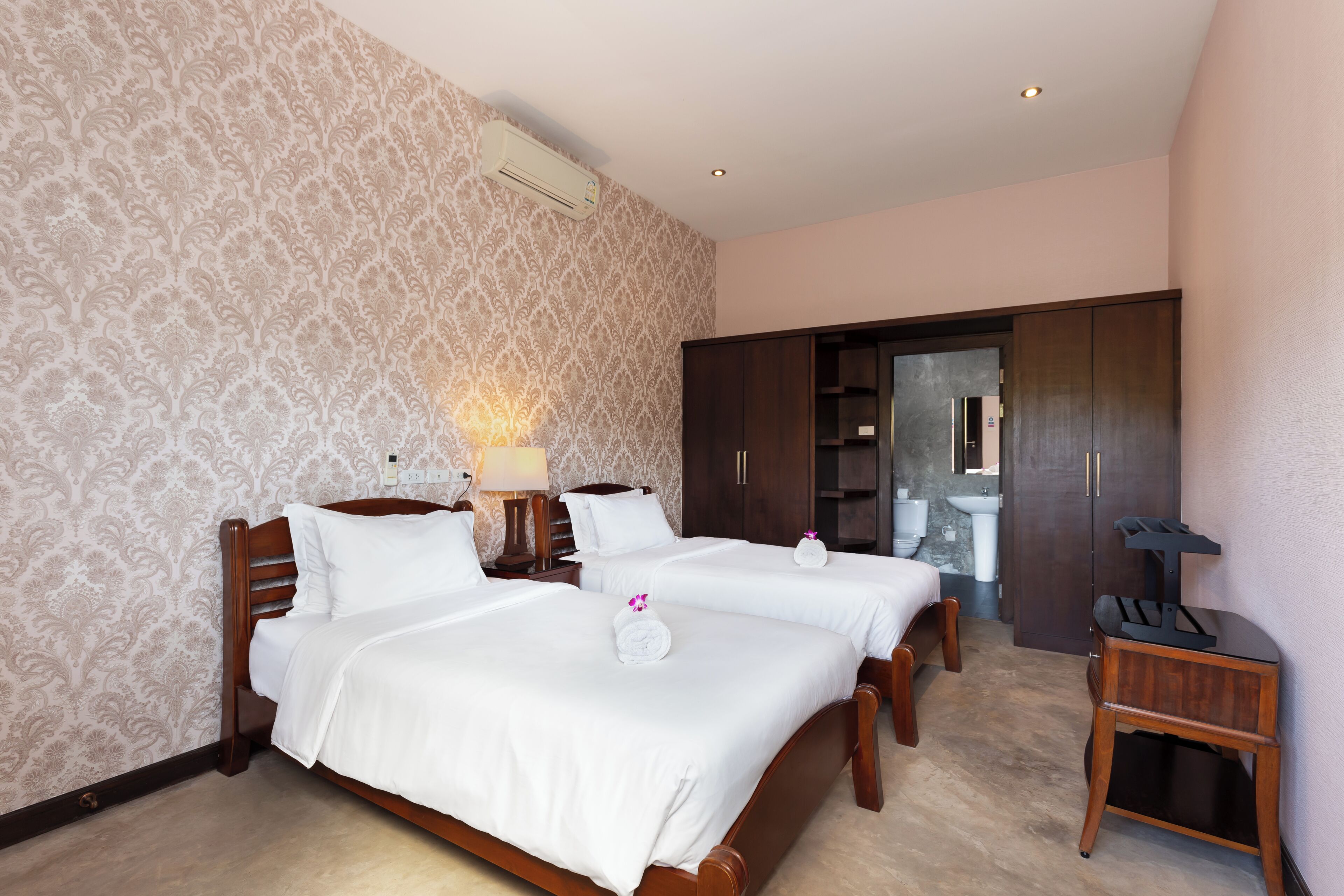 Een hotelkamer met twee bedden, een kledingkast, een bureau en een badkamer die door een open deur zichtbaar is.