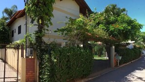 A residential building with a gated entrance, surrounded by lush greenery and a clear sky. - Residencial Cachoeira Flats (Florianópolis)