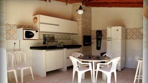 A compact kitchen with white cabinets, a microwave, a sink, and a refrigerator. There is a small dining area with a round table and four chairs. - Residencial Cachoeira Flats (Florianópolis)