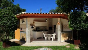 A covered outdoor kitchen area with a dining table and chairs, surrounded by a garden with a patterned walkway. - Residencial Cachoeira Flats (Florianópolis)