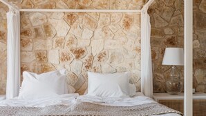 Un lit avec une literie blanche et un mur en pierre en arrière-plan.