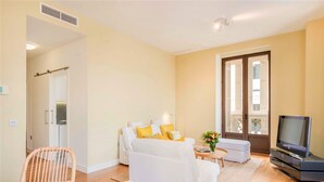 Una sala de estar con sofá, televisión y una zona de comedor con una silla y mesa.