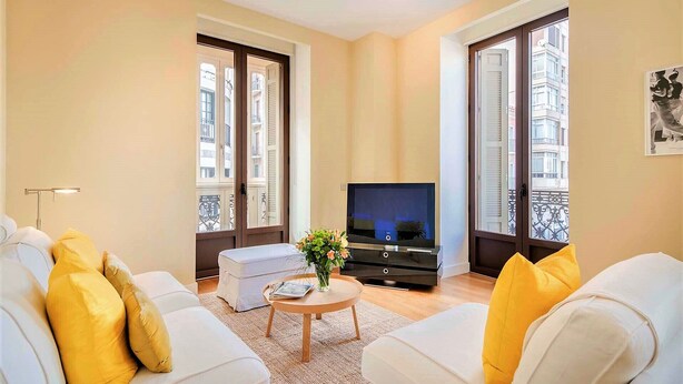 Una sala de estar con un conjunto de sofá, una mesa de centro, un televisor y ventanas grandes con contraventanas.