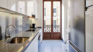 Una cocina estrecha con electrodomésticos de acero inoxidable, un par de puertas con paneles de vidrio decorativos y vistas a edificios cercanos.