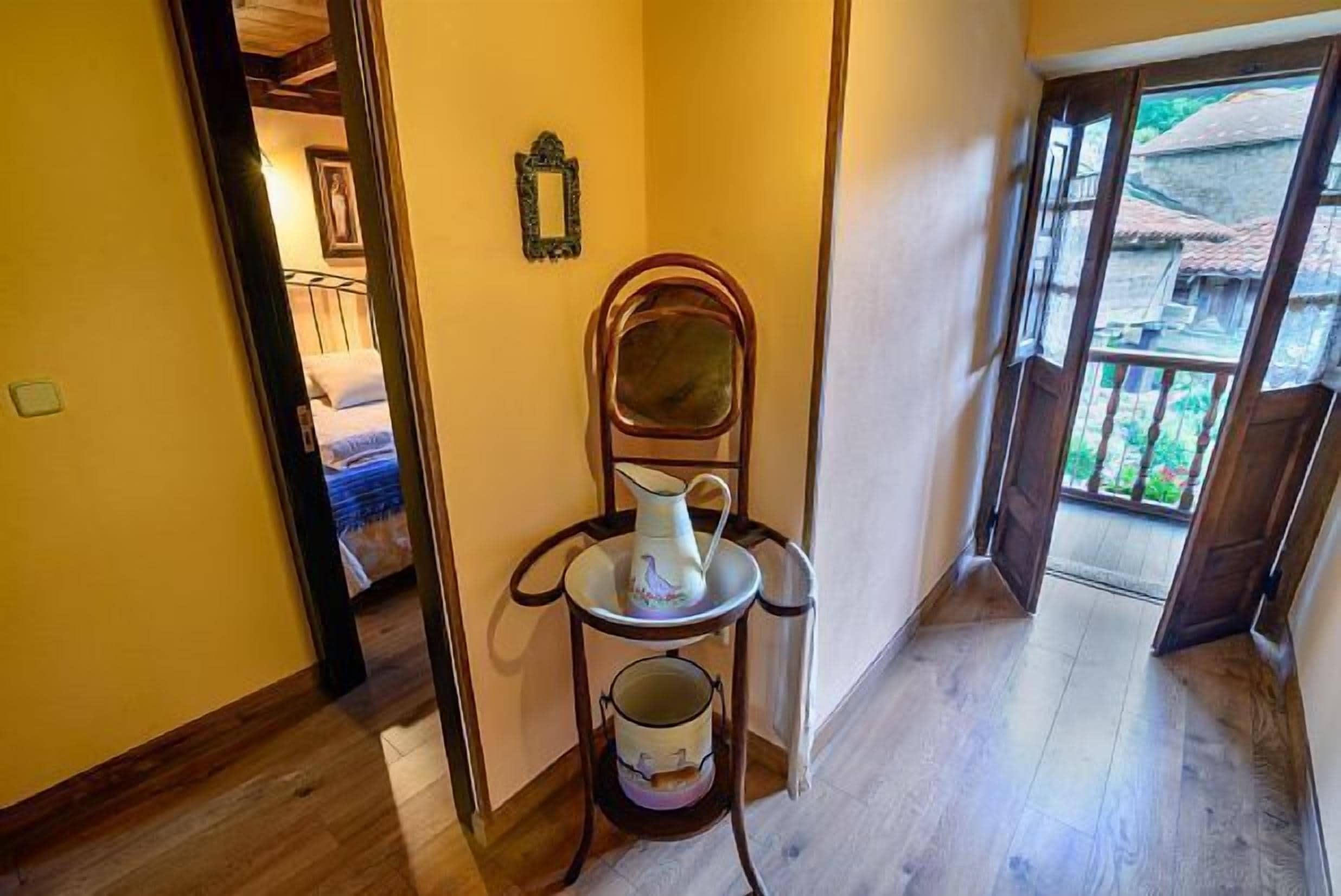 Un couloir étroit au plancher en bois, une petite table avec une carafe et une tasse, et un miroir accroché au mur.