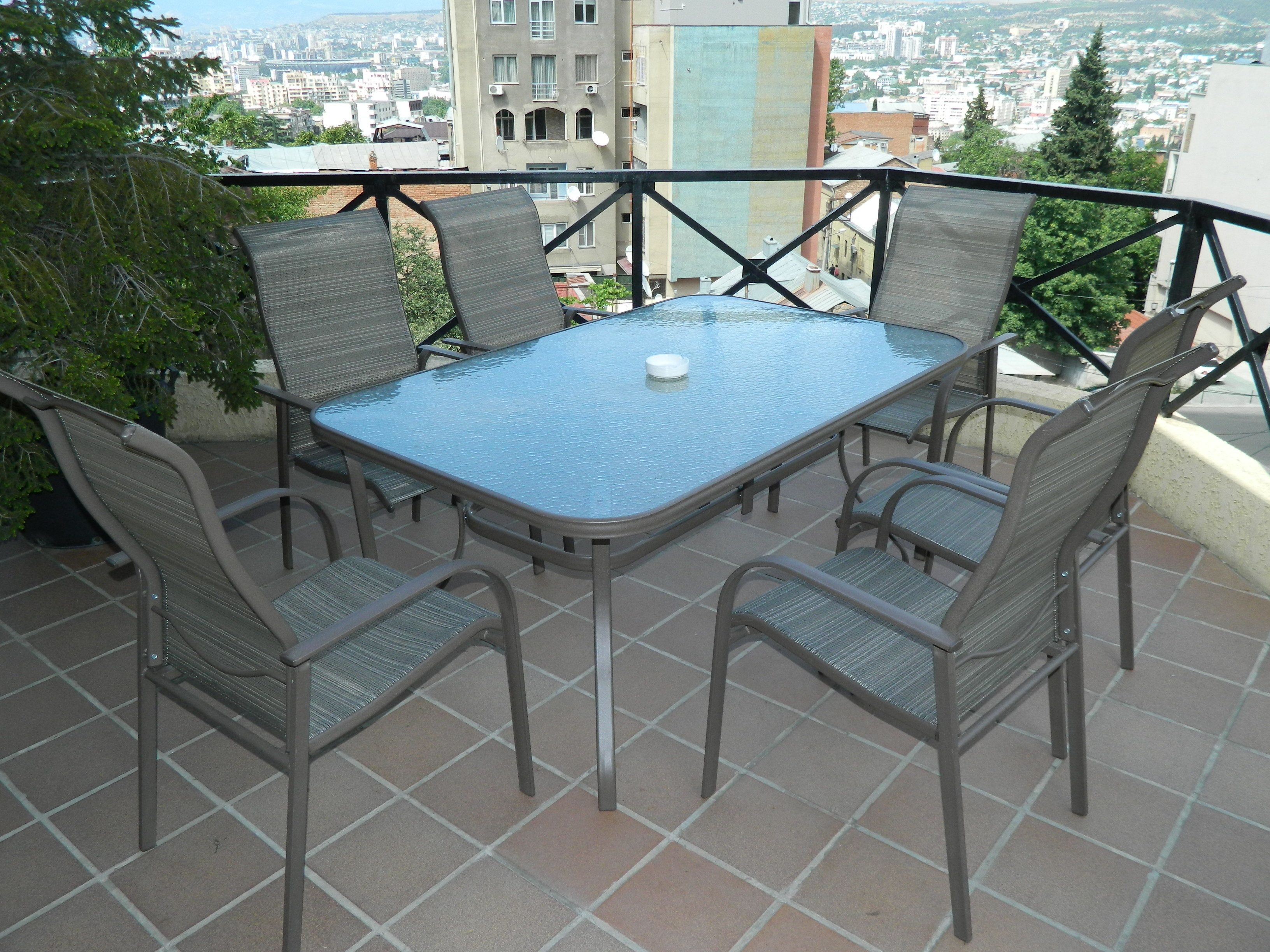 Mesa de vidrio con cuatro sillas en un balcón con vista a la ciudad.