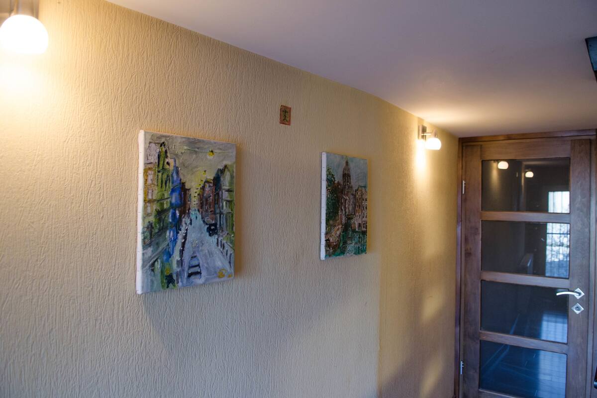 A hallway with two paintings on the wall, a wooden door with glass panels, and a light fixture on the ceiling.