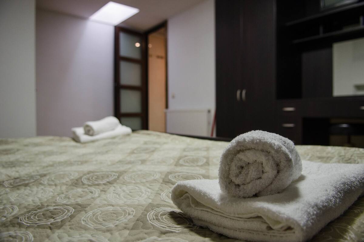 A neatly made bed with a rolled-up towel and a rolled towel on the floor.