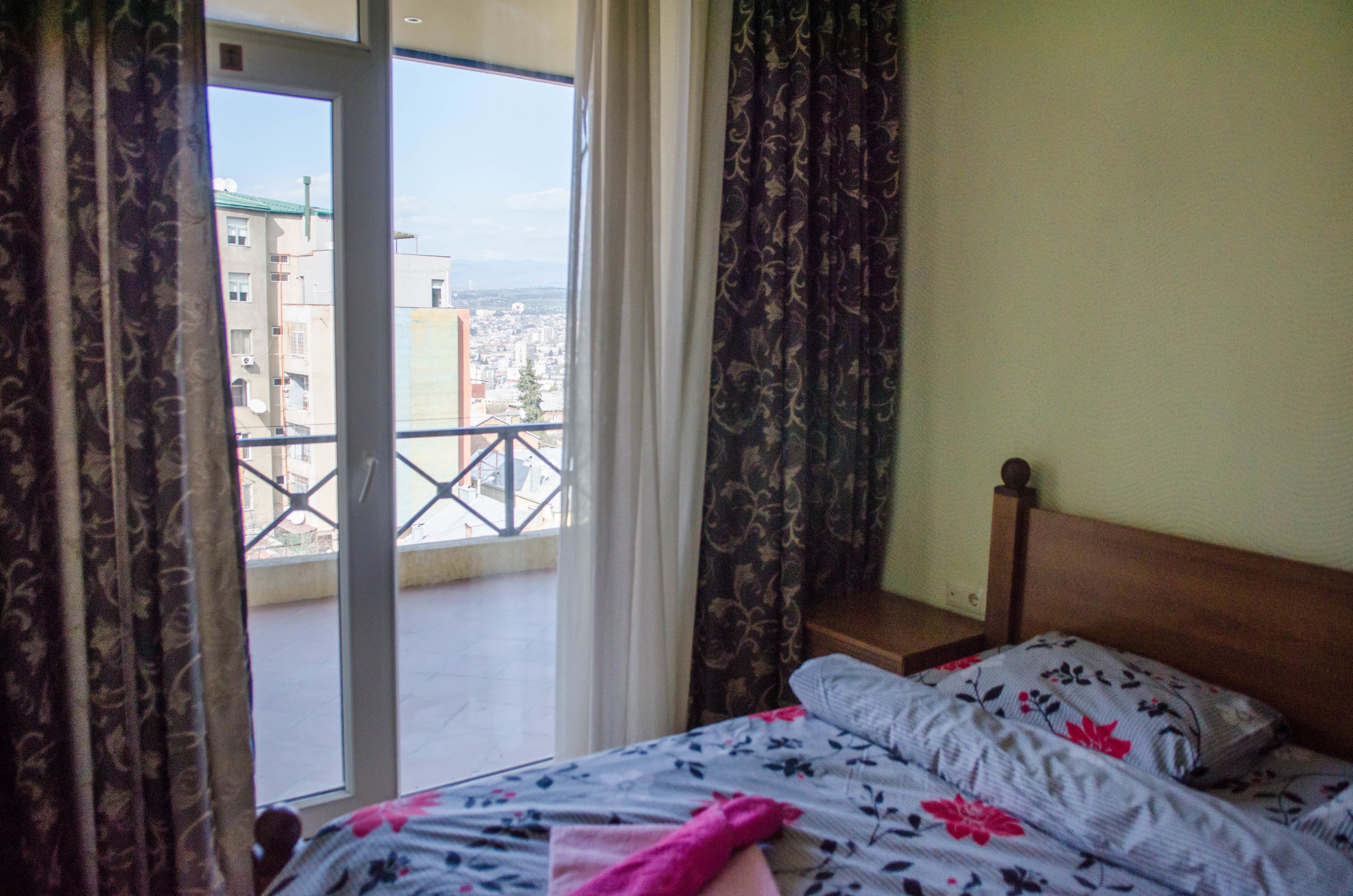A bedroom with a bed, a wooden headboard, and a view through a window to a balcony.