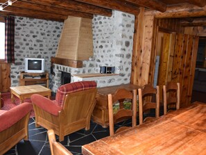 A cozy cabin interior with a stone wall, wooden furniture, a fireplace, and a television.