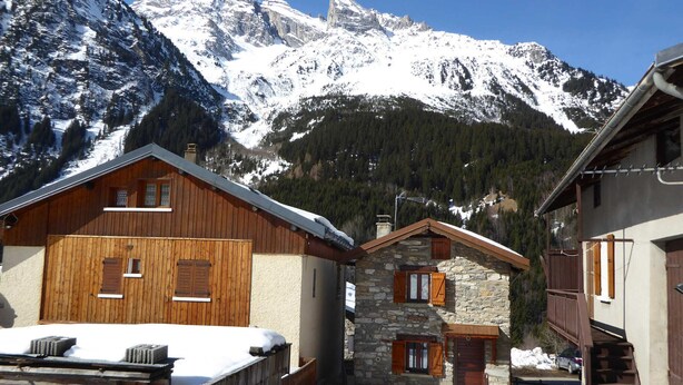 A mountain lodge with wooden cabins, stone buildings, and a snowy mountain backdrop.