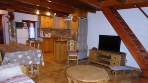 A cozy, well-lit room with a dining table, a sofa, a TV, and a kitchen area.