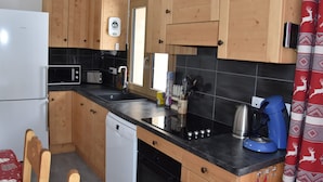 Una cocina compacta con armarios de madera, encimera negra, microondas, lavavajillas y cafetera.