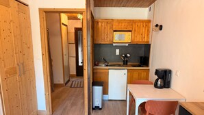 A compact kitchen with wooden cabinets, a microwave, a refrigerator, a sink, and a coffee maker.