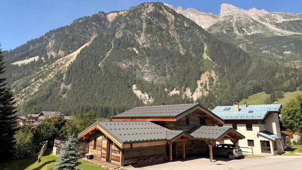 A mountain lodge with a wooden exterior, a covered parking area, and a view of the surrounding mountains.