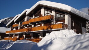 A multi-story wooden building with balconies, surrounded by snow and mountains.