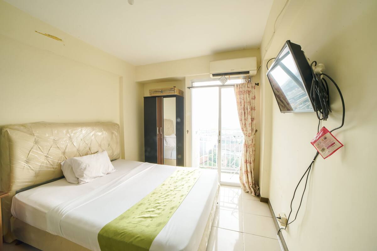 A hotel room with a bed, a wardrobe, a television mounted on the wall, and a window with curtains.