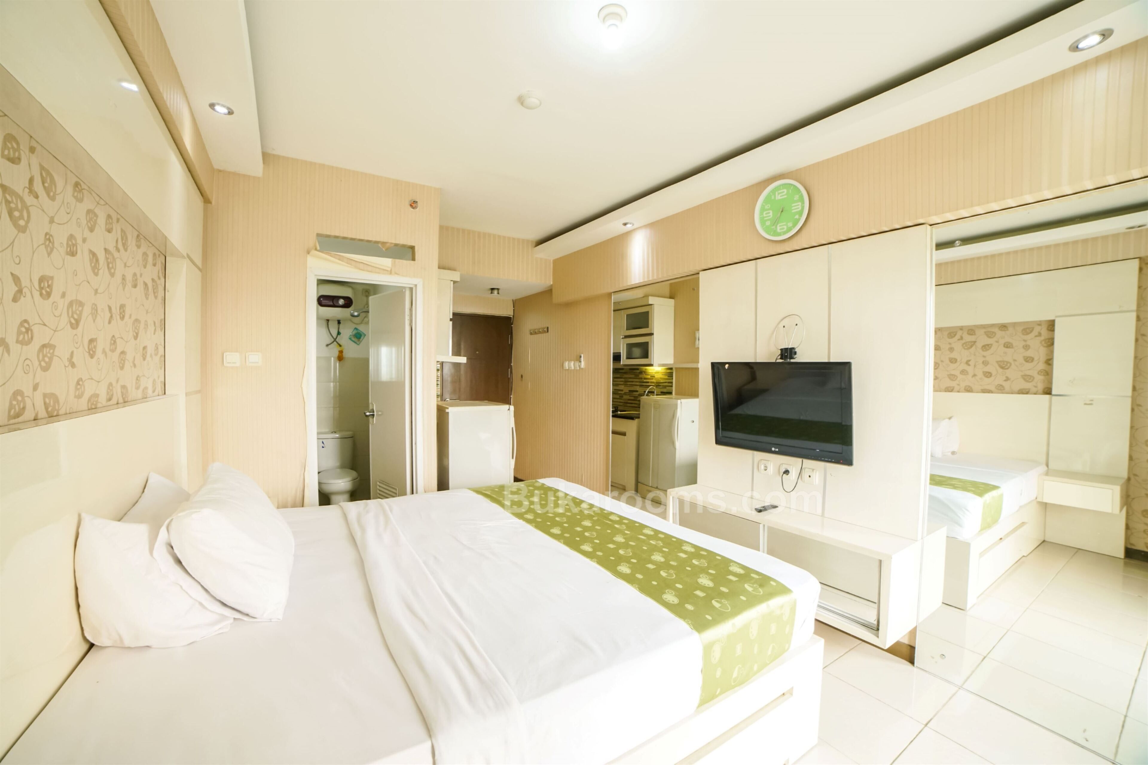 A hotel room with a bed, a TV, a desk, and a bathroom visible through an open door.