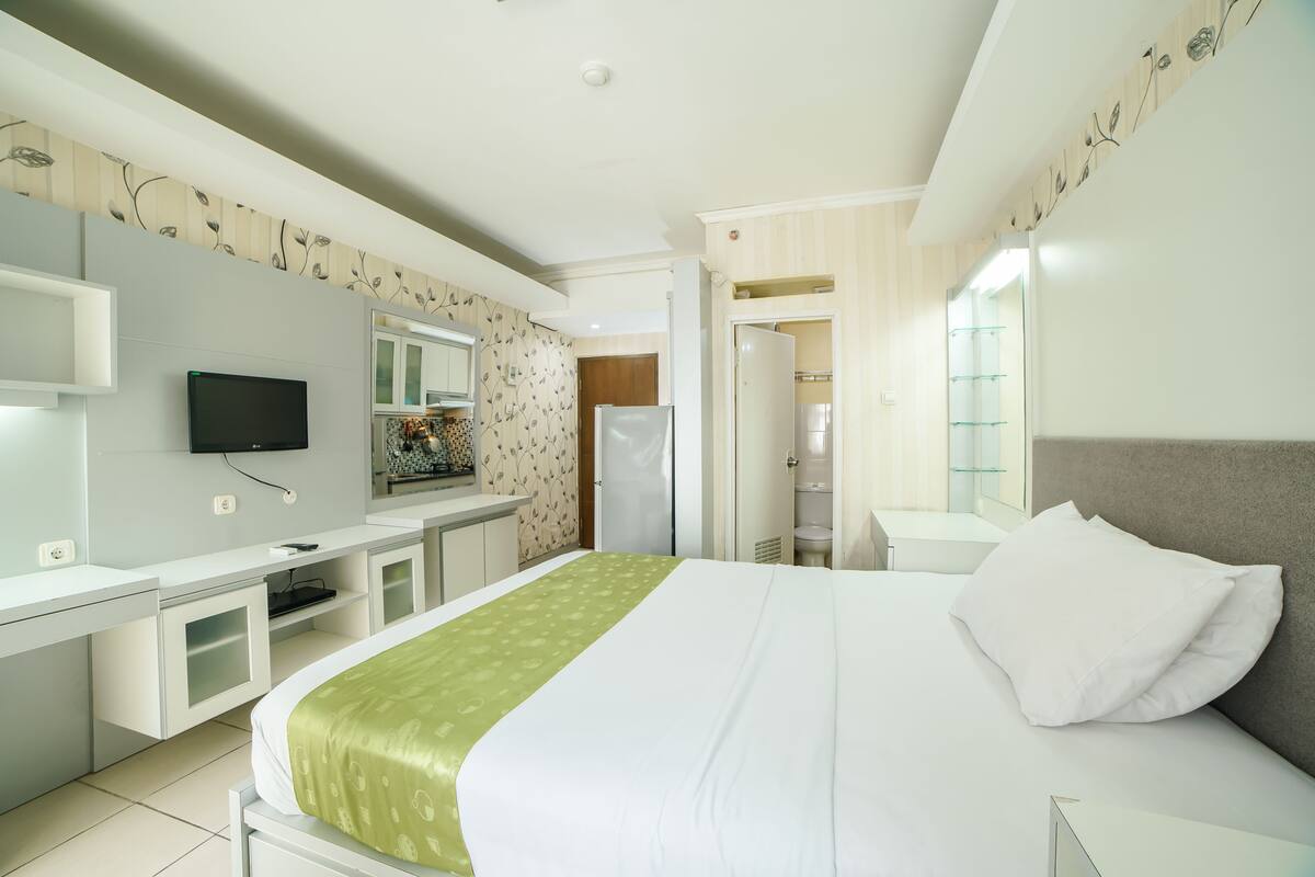 A hotel room with a bed, a desk, a television, and a bathroom visible through an open door.