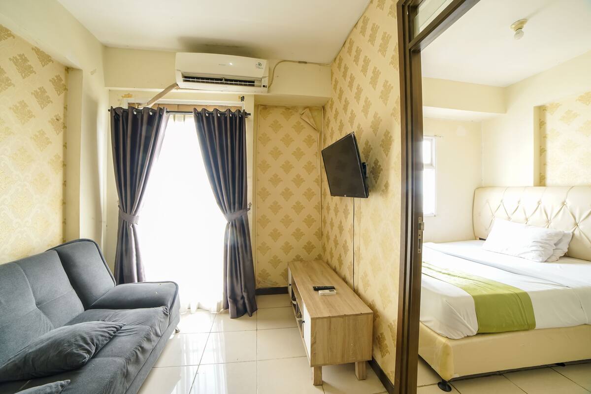 A hotel room with a bed, a sofa, a small wooden table, and a TV mounted on the wall.