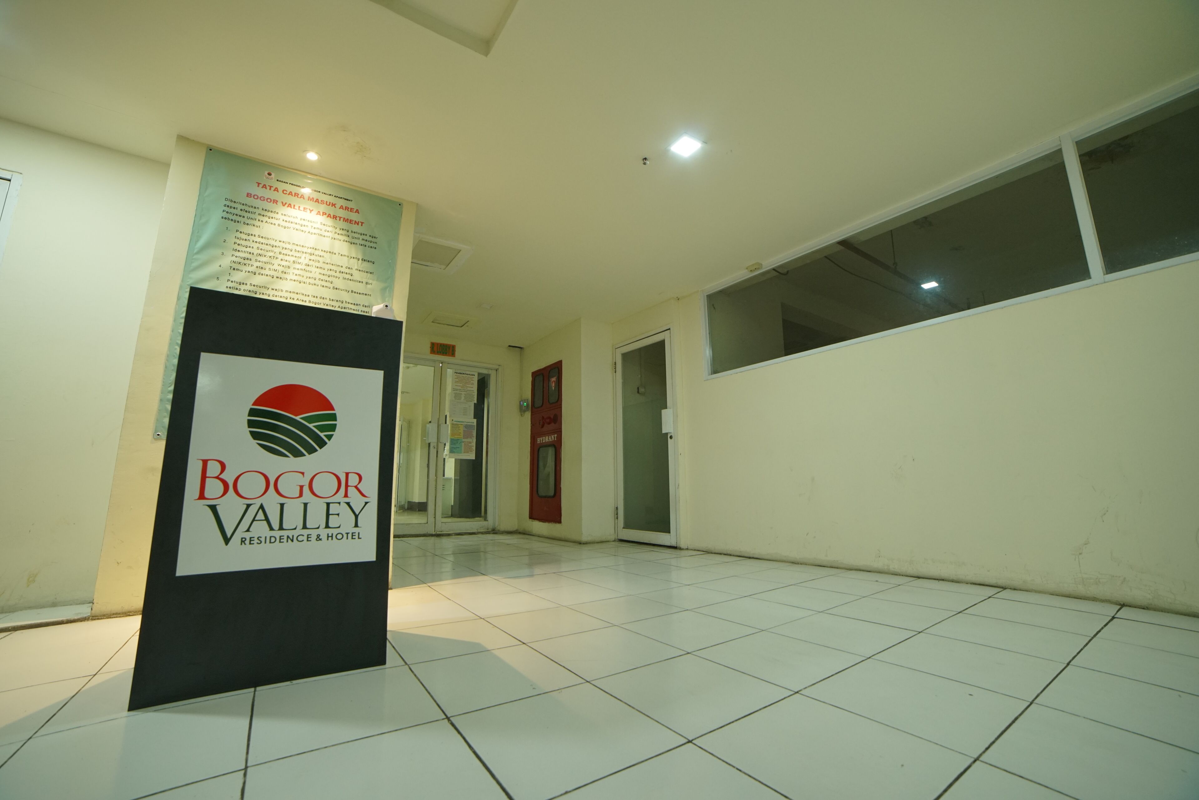 A corridor with a sign for Bogor Valley Residence & Hotel, tiled floor, and a door leading to another room.
