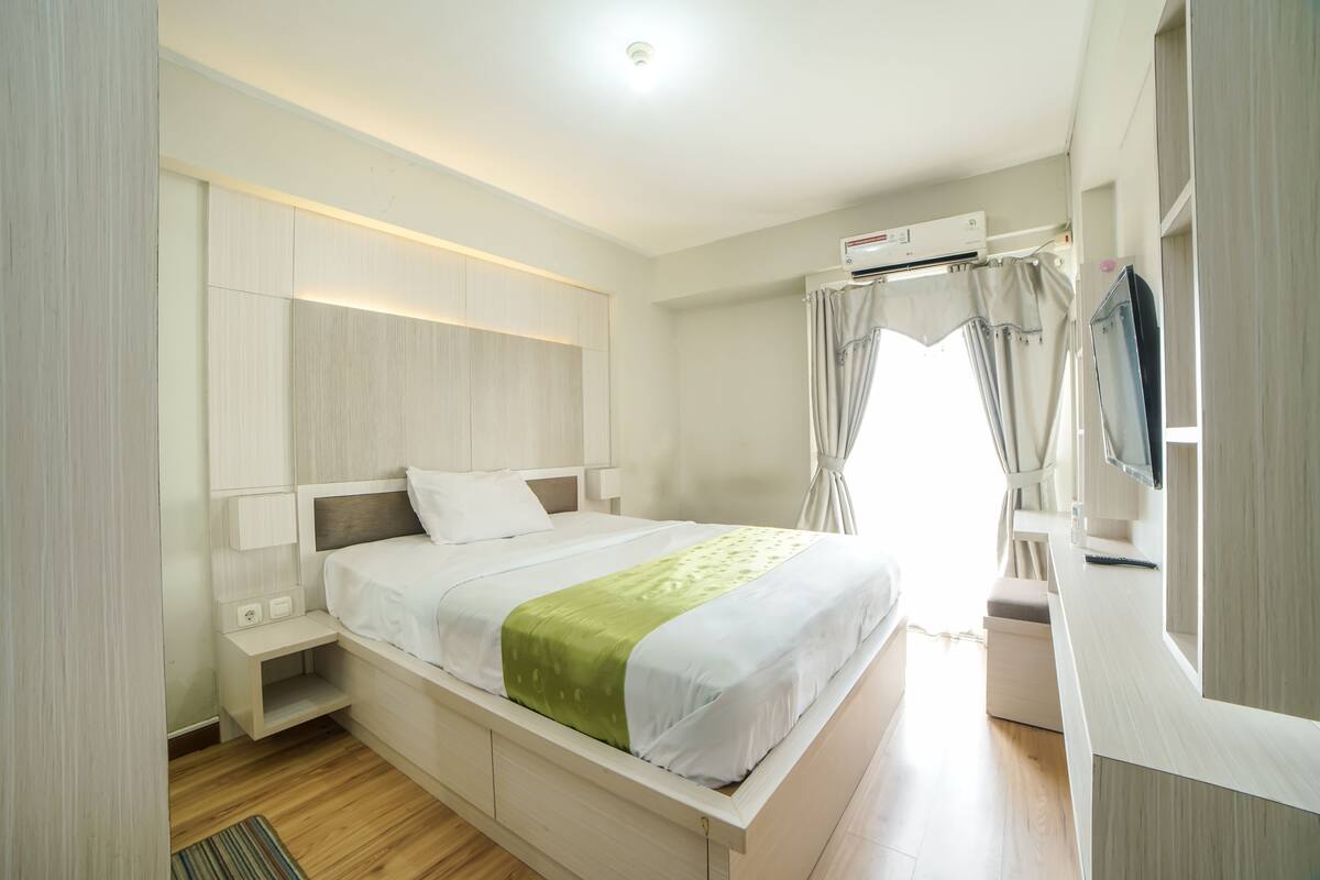 A modern bedroom with a bed, bedside tables, a TV, and an air conditioning unit.