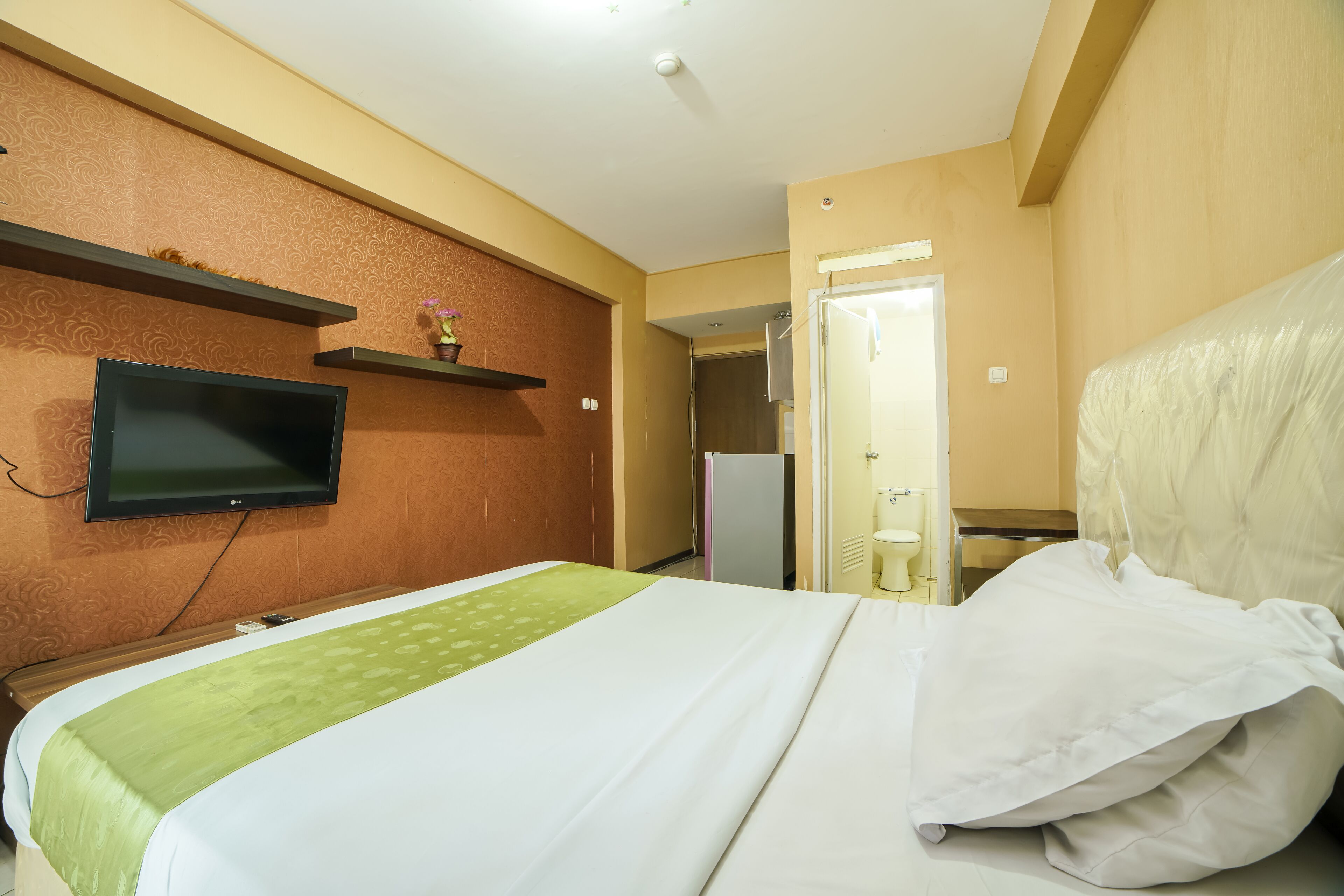 A hotel room with a bed, a television mounted on the wall, and a door leading to a bathroom.