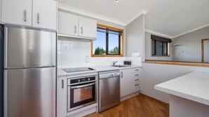 A modern kitchen with stainless steel appliances, white cabinetry, and a large window. - Parkview Apartments (National Park Village)