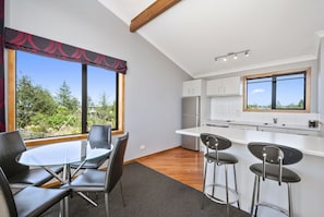 A modern kitchen with white cabinets, a stainless steel refrigerator, and a large window offering a view of trees. - Parkview Apartments (National Park Village)
