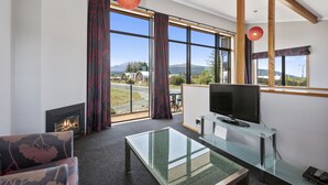 A modern living room with a fireplace, a television, and large windows offering a mountain view. - Parkview Apartments (National Park Village)