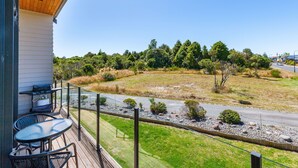 A balcony with a table and chairs, overlooking a grassy area with trees and a road. - Parkview Apartments (National Park Village)