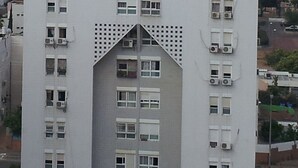 A high-rise building with a unique triangular central section, multiple balconies, and air conditioning units.