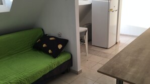 A compact living space with a green sofa, a small table, and a white refrigerator.