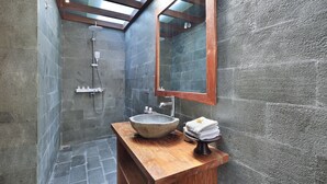 A bathroom with a stone sink, wooden vanity, and a glass-enclosed shower. - Batu Agung Villas (Ubud)