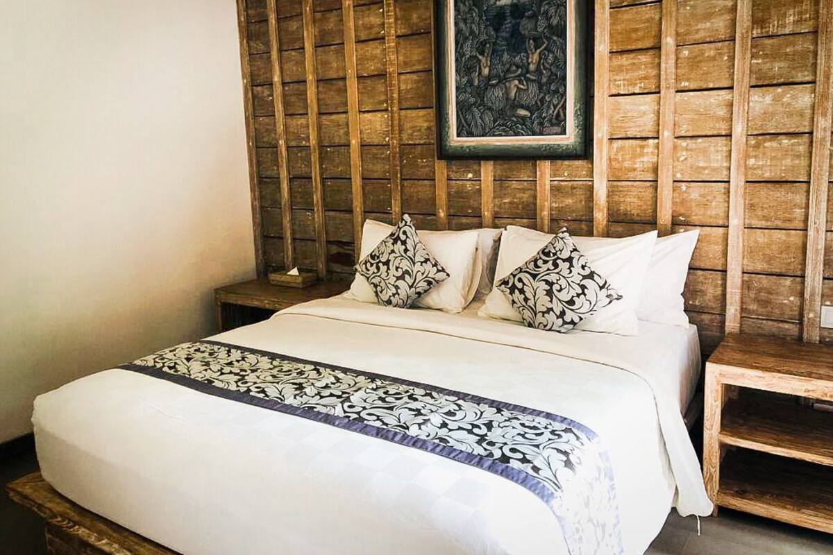 A bedroom with a wooden headboard, a bed with white bedding and patterned pillows, and a framed artwork above the headboard.