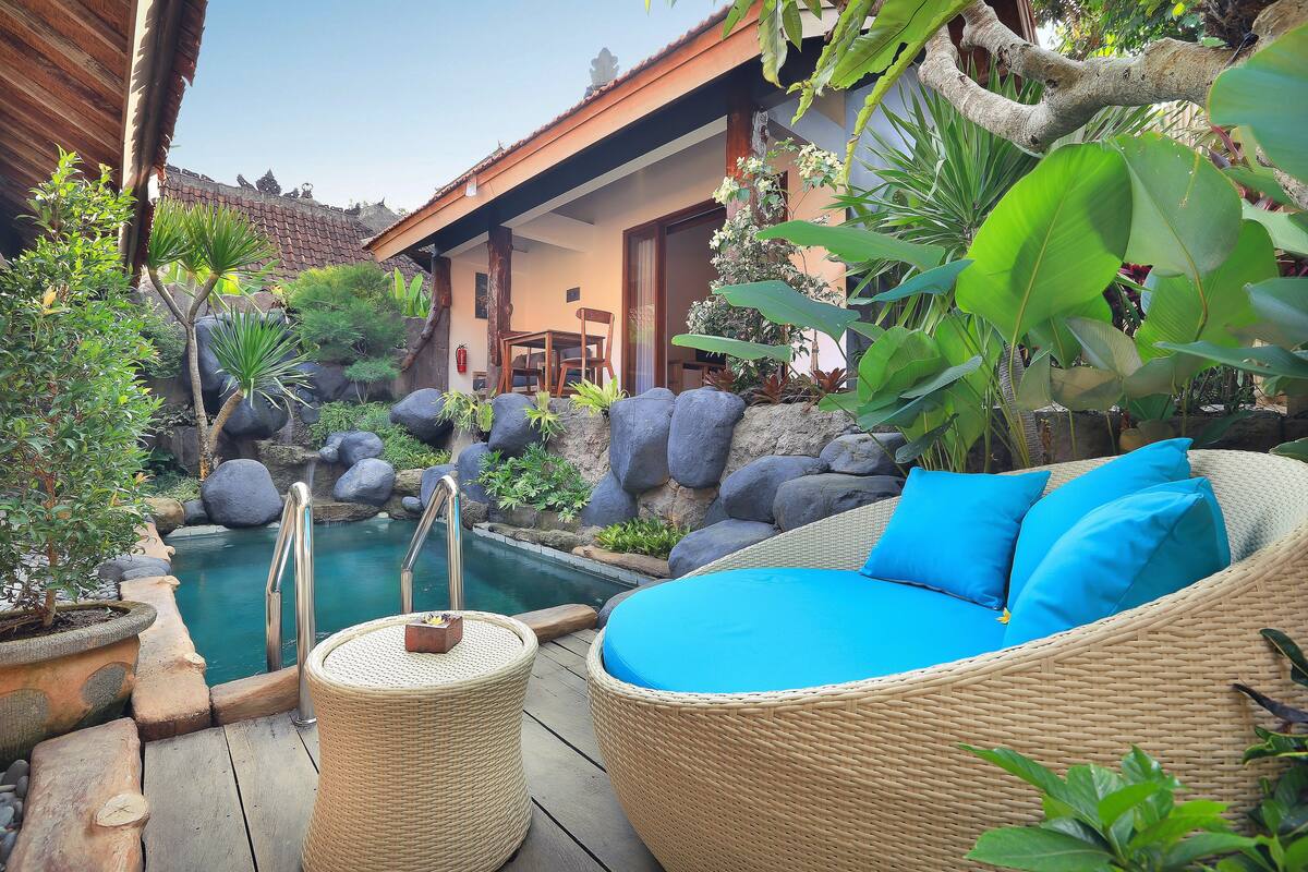 A serene outdoor area with a pool, wicker furniture, and lush greenery.