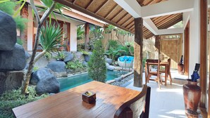 A wooden table with a bowl, surrounded by a pool, rocks, and tropical plants. - Batu Agung Villas (Ubud)